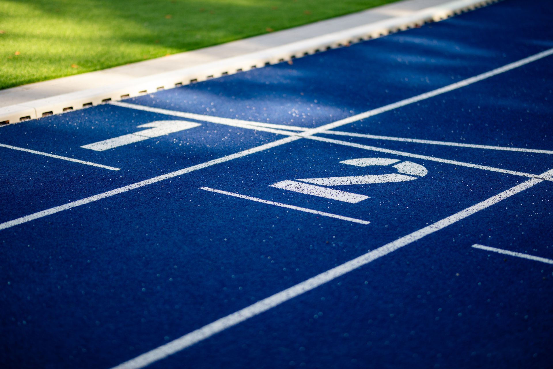 Man sieht eine blaue Laufbahn im Stadion mit weißen Linien und den Zahlen 1 und 2. Die Markierungen zeigen die Startplätze auf der Laufbahn.