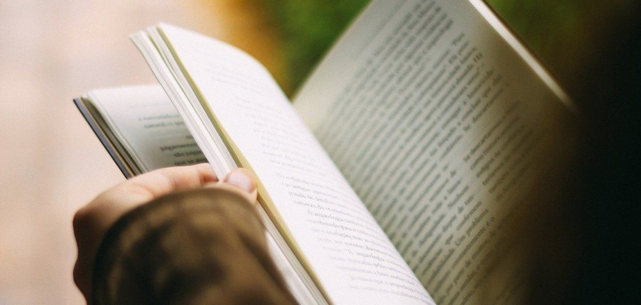 Ein Mann hält ein Buch aufgeschlagen in der Hand und liest darin