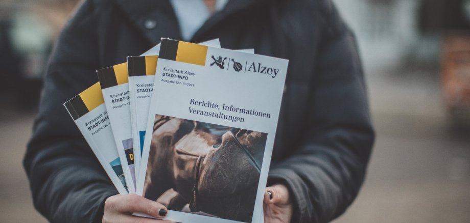 Eine Person hält mehrere Stadt-Infos in die Kamera