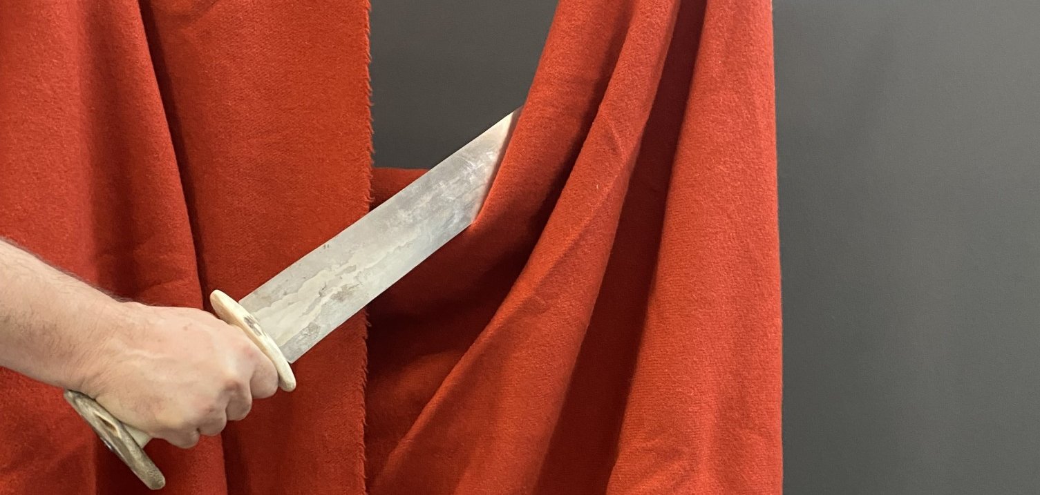 Jemand hält ein Holzschwert in der Hand, der ein rotes Teil Stoff bildlich teilt.