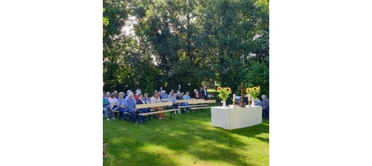 viele Mesnchen sitzen vor einem weiß gekleideten Tisch mit einem Kreuz drauf