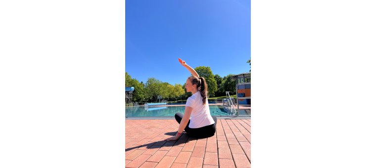 Yoga im Wartbergbad Alzey, zu sehen ist eine Frau die am Pool sitzt und eine Yoga Übung macht.