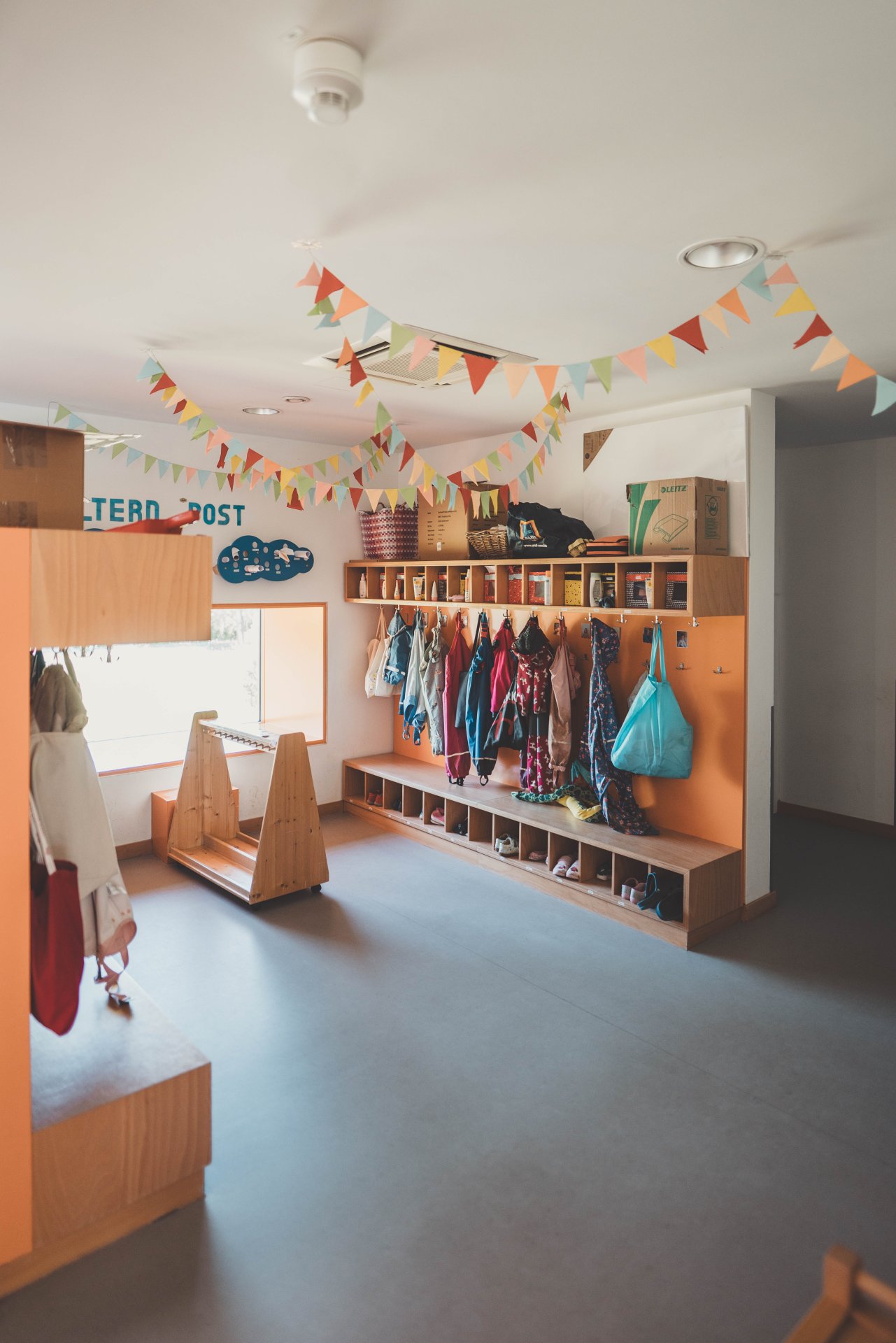 An einer Kindergartengarderobe aus hellem Holz im Flur hängen viele bunte Jacken und Taschen.
