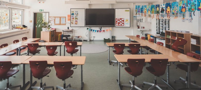 Ein Klassenraum, in dem rote Stühle an den Schultischen stehen.