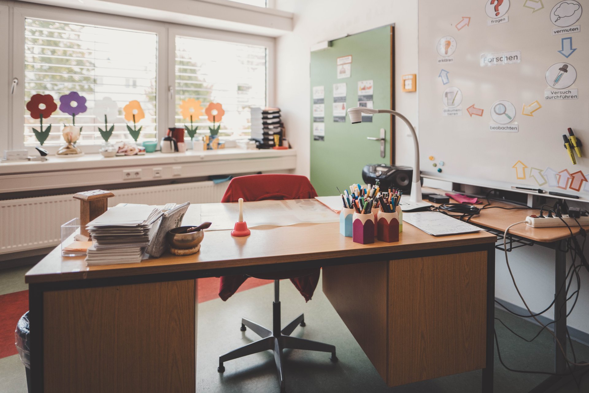 Lehrerpult mit bunten Stiften darauf in einem Klassenzimmer.