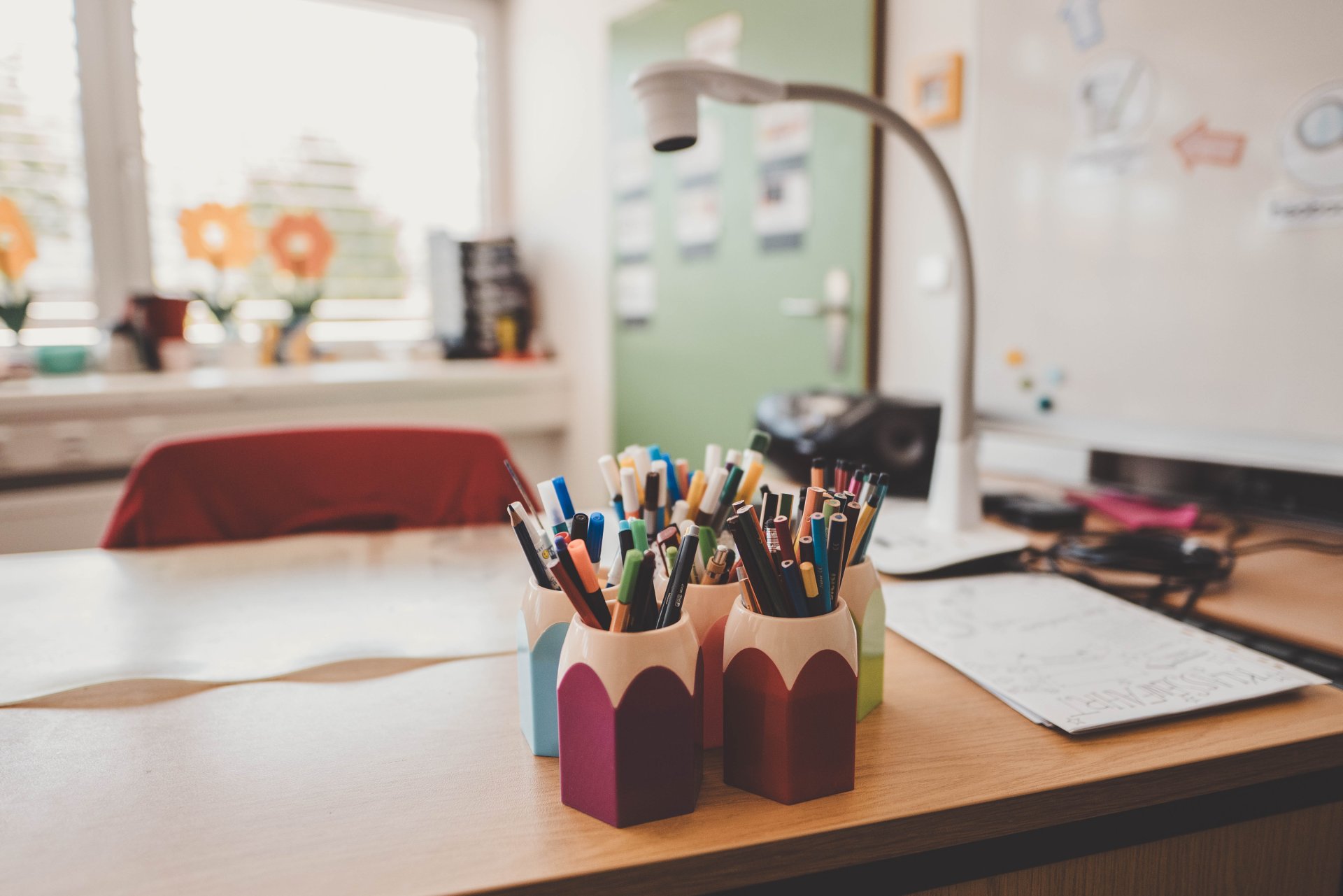Lehrerpult mit bunten Stiften darauf in einem Klassenzimmer in Nahaufnahme.
