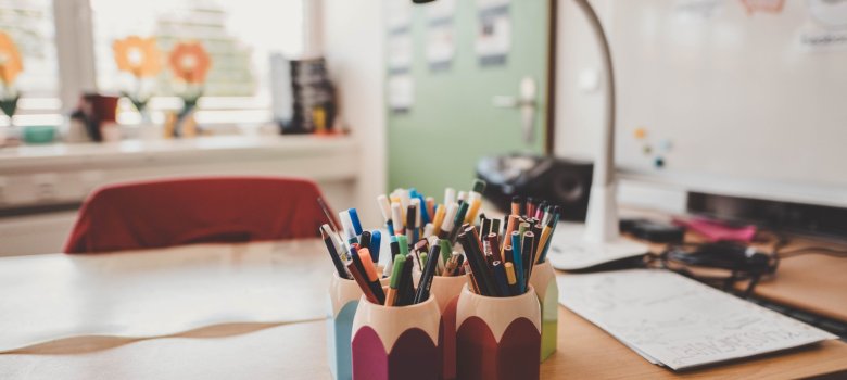 Lehrerpult mit bunten Stiften darauf in einem Klassenzimmer in Nahaufnahme.