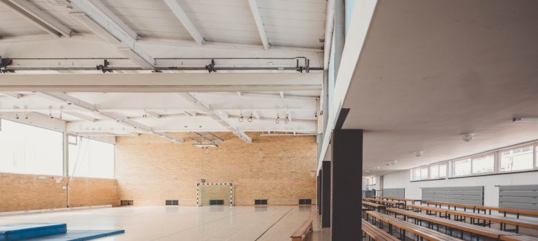Turnhalle mit einer Sitztribüne rechts im Bild und einer blauen Turnmatte in der Mitte der Halle.
