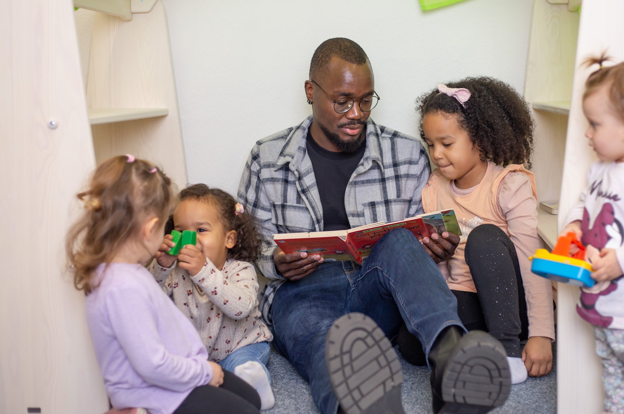 Vater sitzt mit den Kindern auf dem Boden und liest Bücher vor