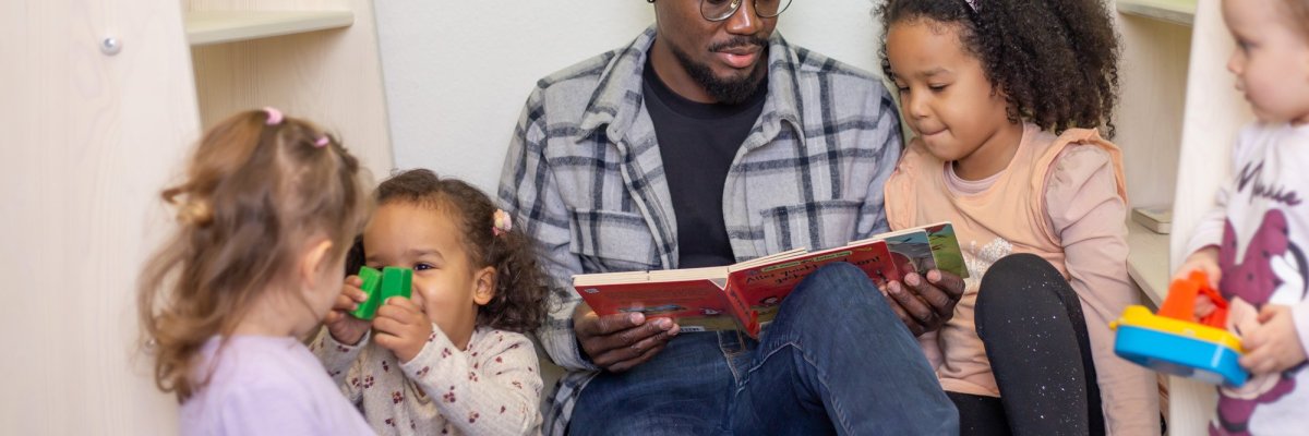 Vater sitzt mit den Kindern auf dem Boden und liest Bücher vor