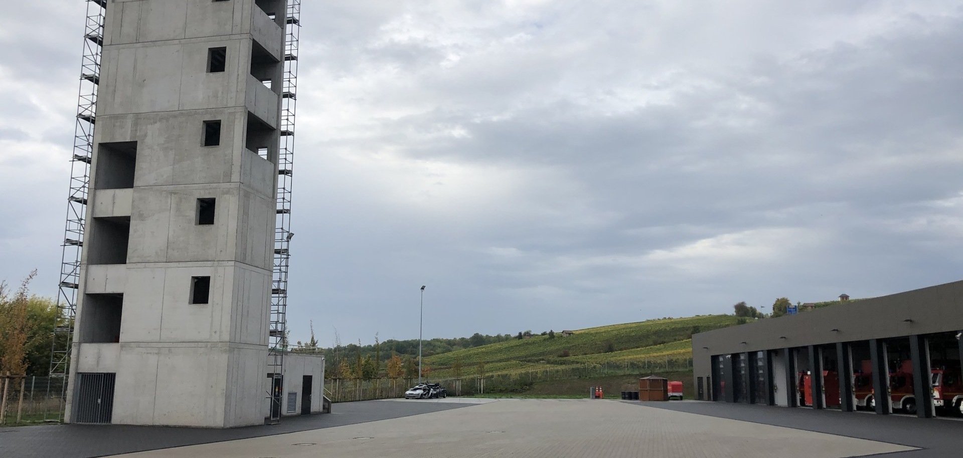 
Auf der linken Seite der 25 Meter hohe Ausbildungsturm mit entsprechenden Anleitermöglichkeiten für tragbare Leitern und die Drehleiter. Außerdem verfügt der Turm über eine Steigleitung, einen Kellerbereich und eine "heiße Tür" für die Atemschutzausbildung.

