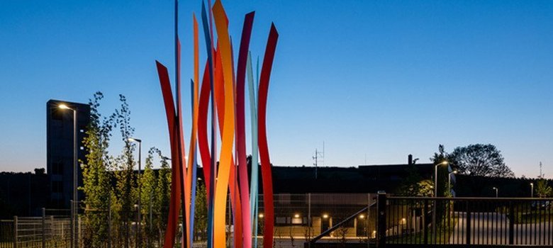 Am Haupteingang der Feuerwache ist ein rotes und blaues skulpturales Farbenspiel sichtbar. Von der einen Seite stellt die Skulptur Wasser und von der anderen Seite Feuer dar.