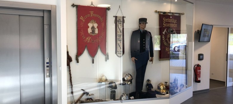 Blick auf die Vitrine im Flurbereich. Hier finden Sie Ausstellungsstücke über die Geschichte der Feuerwehr Alzey und unserer Partnerfeuerwehren.
