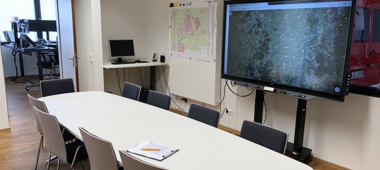 Kleiner Stabsraum und Nebenraum der FEZ. Dieser Raum ist bei Einsätzen Aufenthaltsraum für die Bereitschaftskräfte, kann bei größeren Einsätzen als FEZ Stabsraum genutzt werden. Im Alltag ist hier Platz für Besprechungen bis 10 Personen. Das fahrbare Smartboard wird im Einsatzfall als Unterstützung für die FEZ genutzt, kann aber ebenso für Ausbildungszwecke gebraucht werden. Der Raum verfügt außerdem über einen TV und einen Beamer Kleiner Stabsraum und Nebenraum der FEZ. Dieser Raum ist bei Einsätzen Aufenthaltsraum für die Bereitschaftskräfte, kann bei größeren Einsätzen als FEZ Stabsraum genutzt werden. Im Alltag ist hier Platz für Besprechungen bis 10 Personen. Das fahrbare Smartboard wird im Einsatzfall als Unterstützung für die FEZ genutzt, kann aber ebenso für Ausbildungszwecke gebraucht werden. Der Raum verfügt außerdem über einen TV und einen Beamer