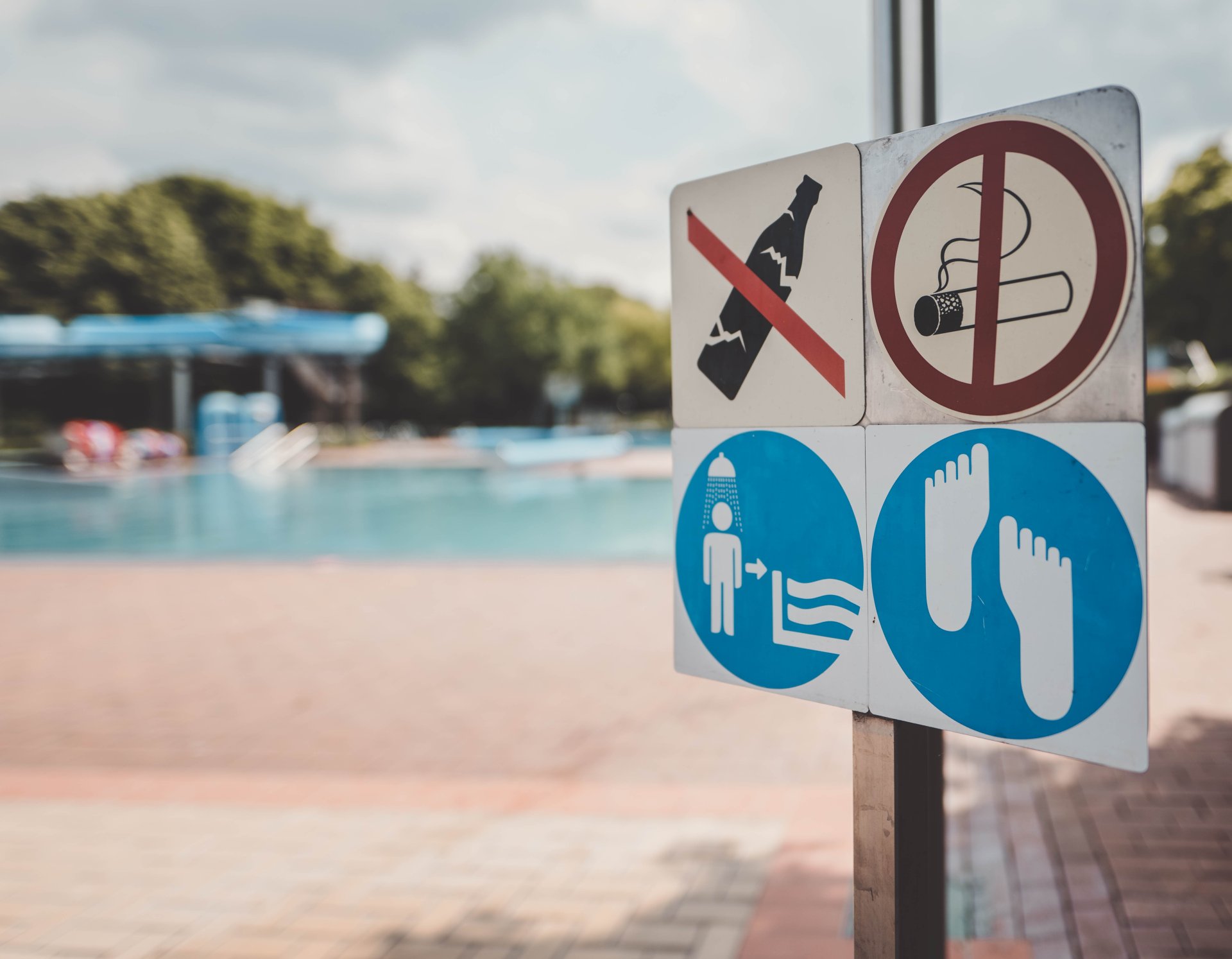 Ein Hinweisschild steht im Vordergrund des Bildes. Im Hintergrund ist verschwommen ein Becken des Alzeyer Freibads.