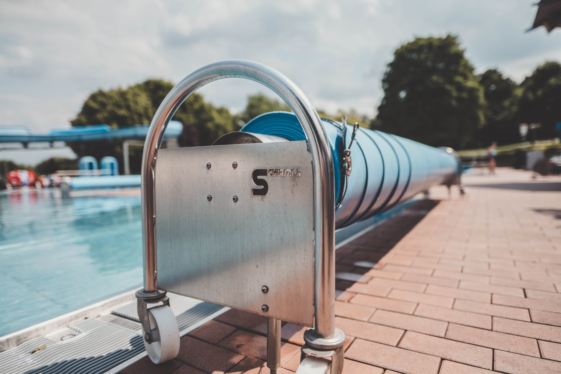 Auf dem Bild ist ein Schwimmbecken des Alzeyer Freibads abgebildet, welches vom beckenrand aus fotografiert wurde. Im Hintergrund sieht man die blaue Rutsche.