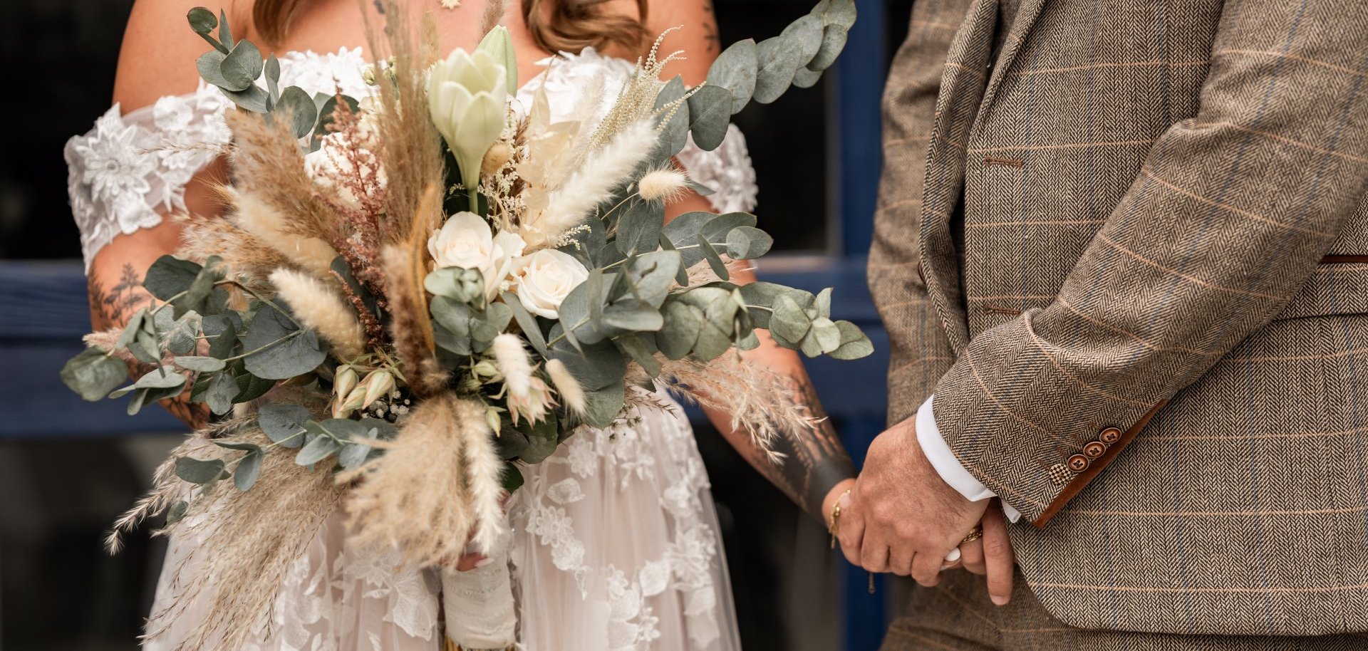 Brautpaar nebeneinander in Anzug und Kleid mit Brautstrauß in der Hand