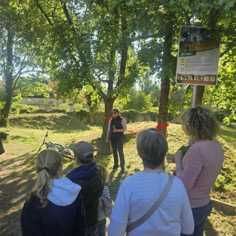 mehrere Personen hören einer Frau zu, die vor ihnen eine Ansprache vor dem neuen Dirtpark hält