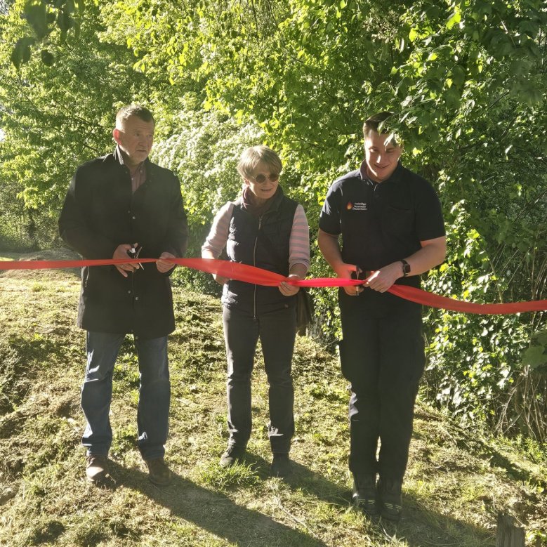zwei Männer und eine Frau stehen vor einem roten Band und schneiden dieses gemeinsam durch