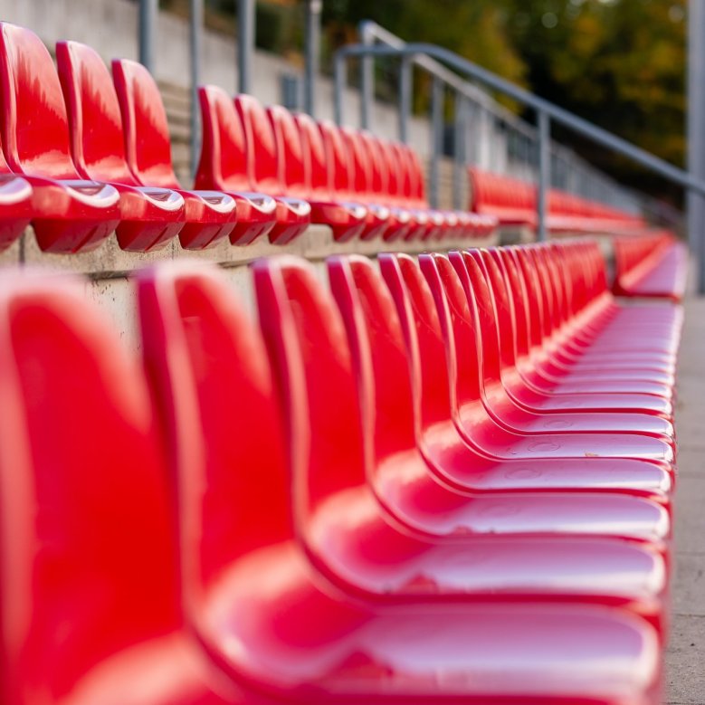 Auf dem Bild sind die roten Sitzschalen der trebühne des Alzeyer Wartbergstadions abgebildet.