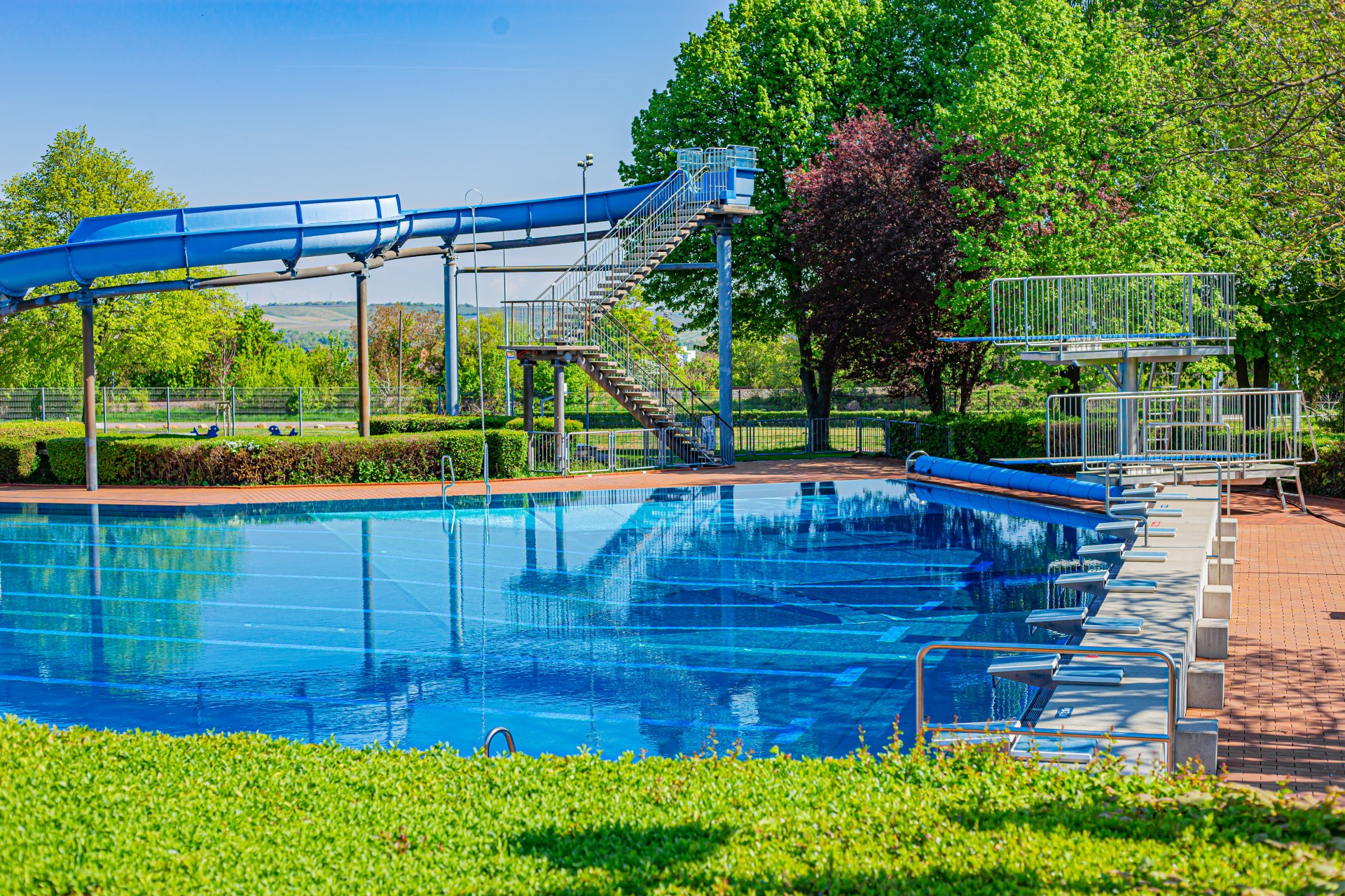 Sicht auf das Schwimmbecken, das ein Meter-Brett sowie das Drei-Meter-Brett und die lange blaue Rutsche.