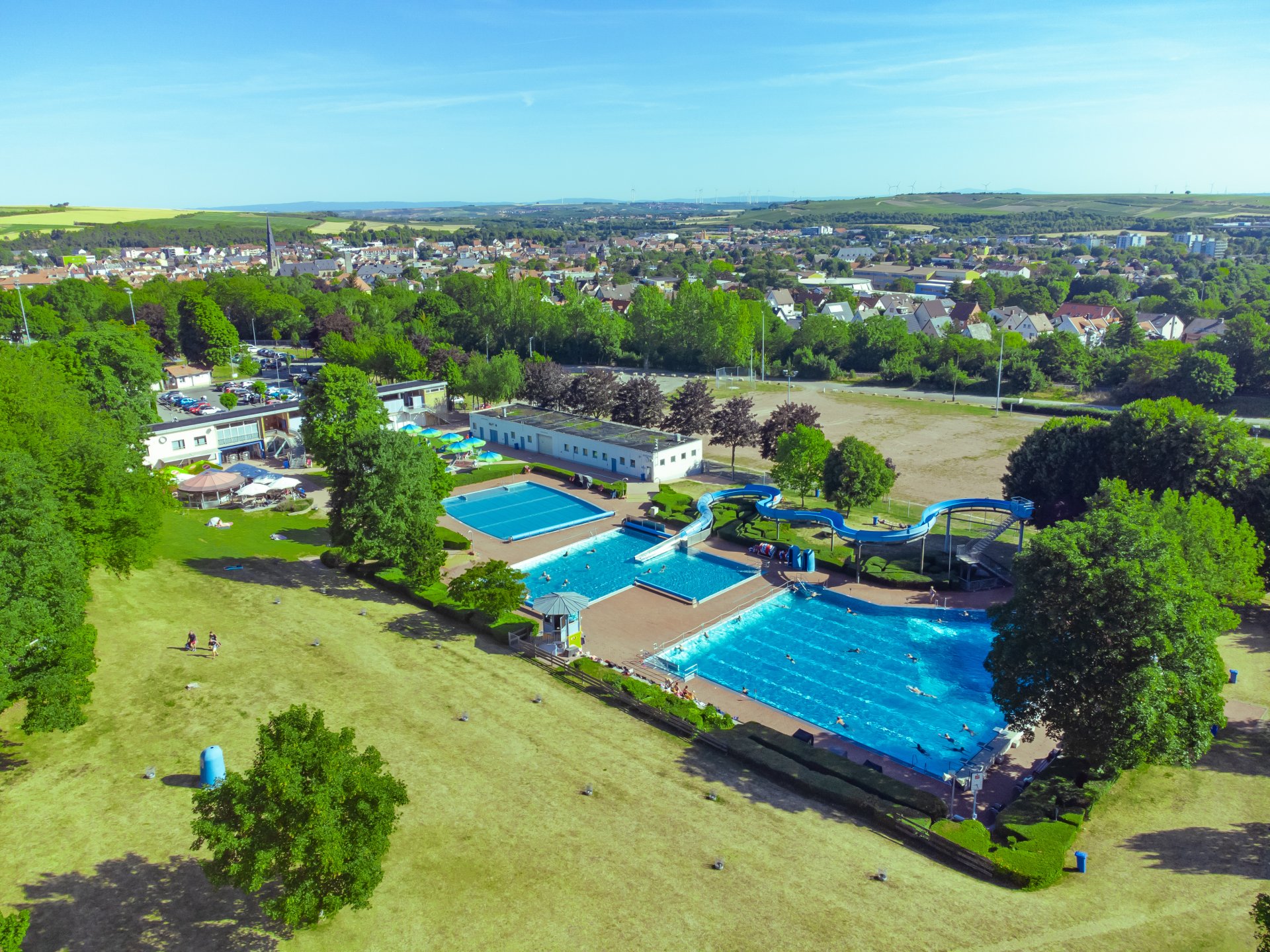 Das gesamte Freibad aus der Vogelperspektive, mit allen drei Becken sowie der Wiese und den Essensbereichen.