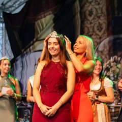 Zwei Frauen stehen auf einer Bühne. Die hintere setzt der vorderen eine Krone auf den Kopf. Bürgermeister Steffen Jung steht daneben.