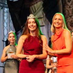 Zwei Frauen stehen auf einer Bühne nebeneinander und lachen in die Zuschauermenge.