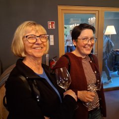 zwei Frauen mit einem glas Wein in der Hand lachen gemeinsam in die Kamera