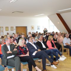 mehrere Menschen sitzen in einem Saal in Stuhlreihen und hören gespannt zu