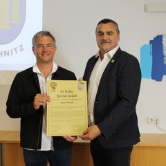 die beiden Bürgermeister aus Alzey und aus Rechnitz halten gemeinsam eine Urkunde in die Kamera, worauf steht: 45 Jahre Partnerschaft