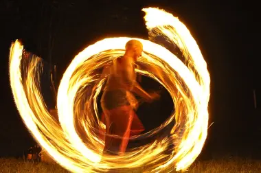 ein Mann dreht Feuerfackeln so schnell neben sich her, dass sich auf dem Bild ganze Feuerkreise ergeben