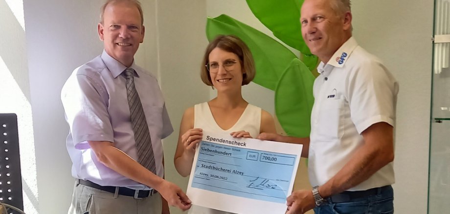 Gernot Marx (r.) überreicht den Spendenscheck an Katharina Moeske (m.) und Bürgermeister Burkhard (l.) Die Stadtbücherei erhält eine großzügige Spende