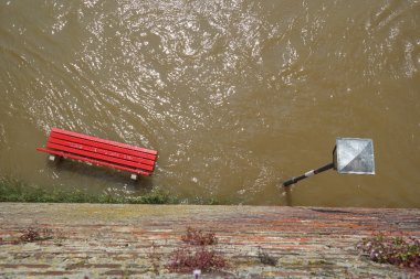 Überfluteter Weg mit einer roten Bank und einer Laterne