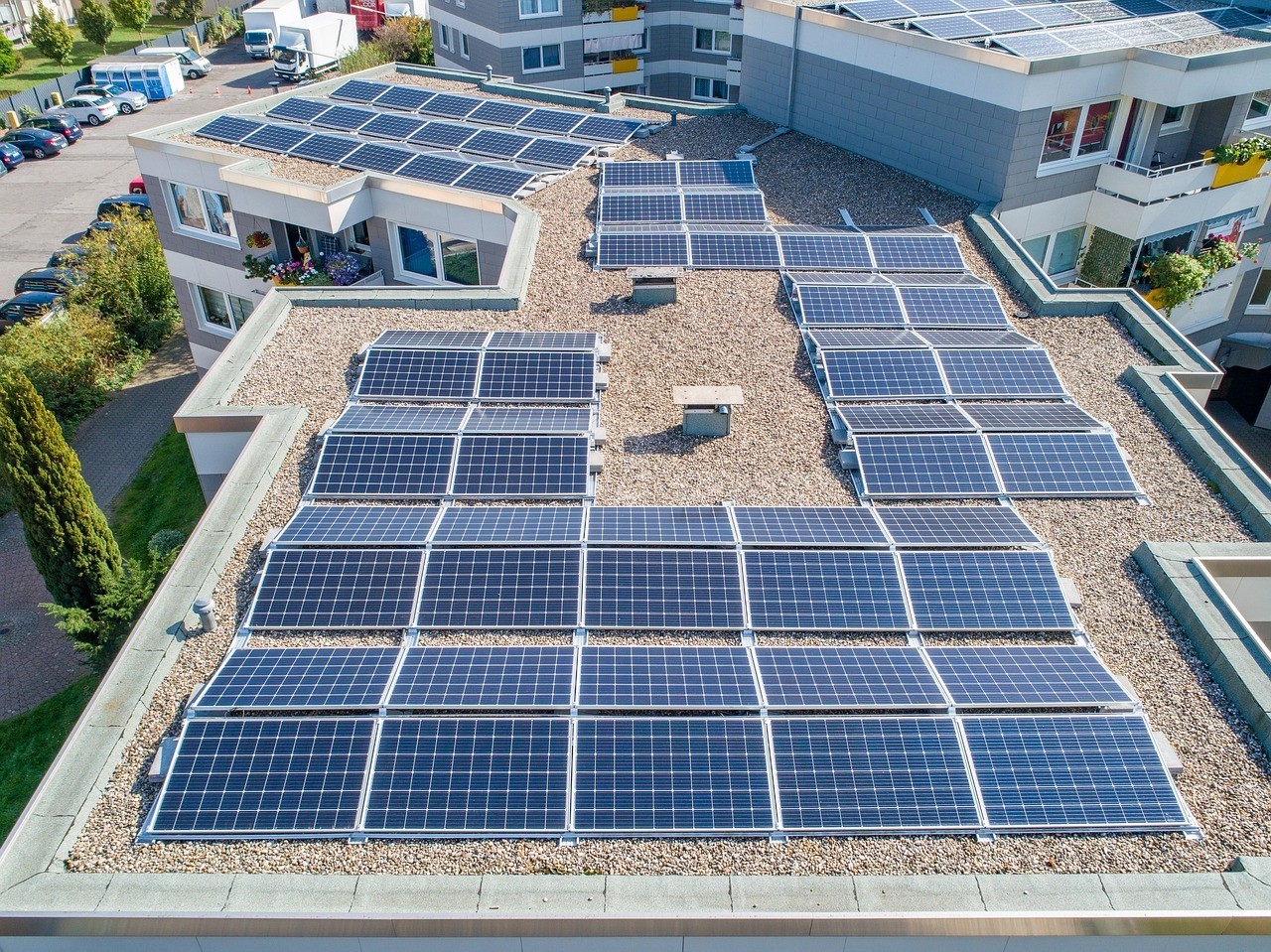 Ein Dach eines Mehrfamilienhauses mit zahlreichen Solarplatten aus der Luft fotografiert.