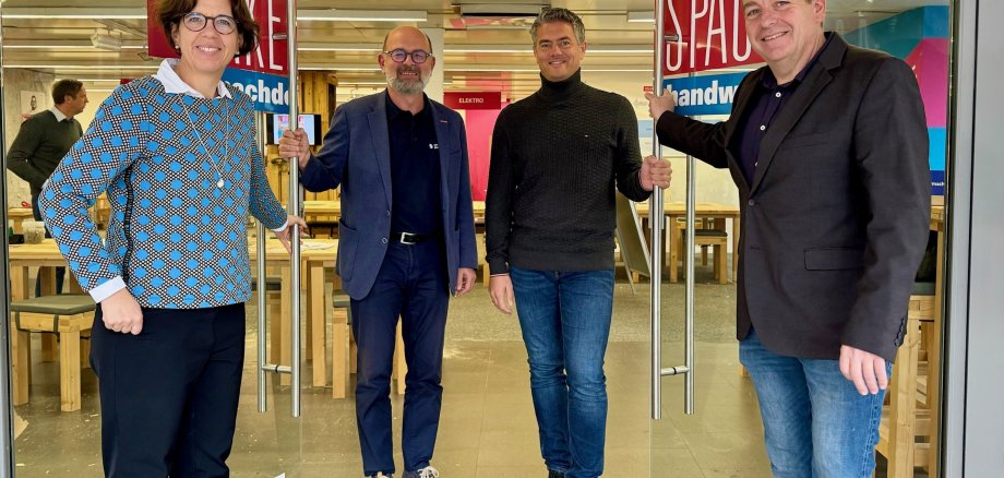 Vier Personen stehen vor einer offenen Glastür zu einem Raum mit zahlreichen Holzmöbeln.