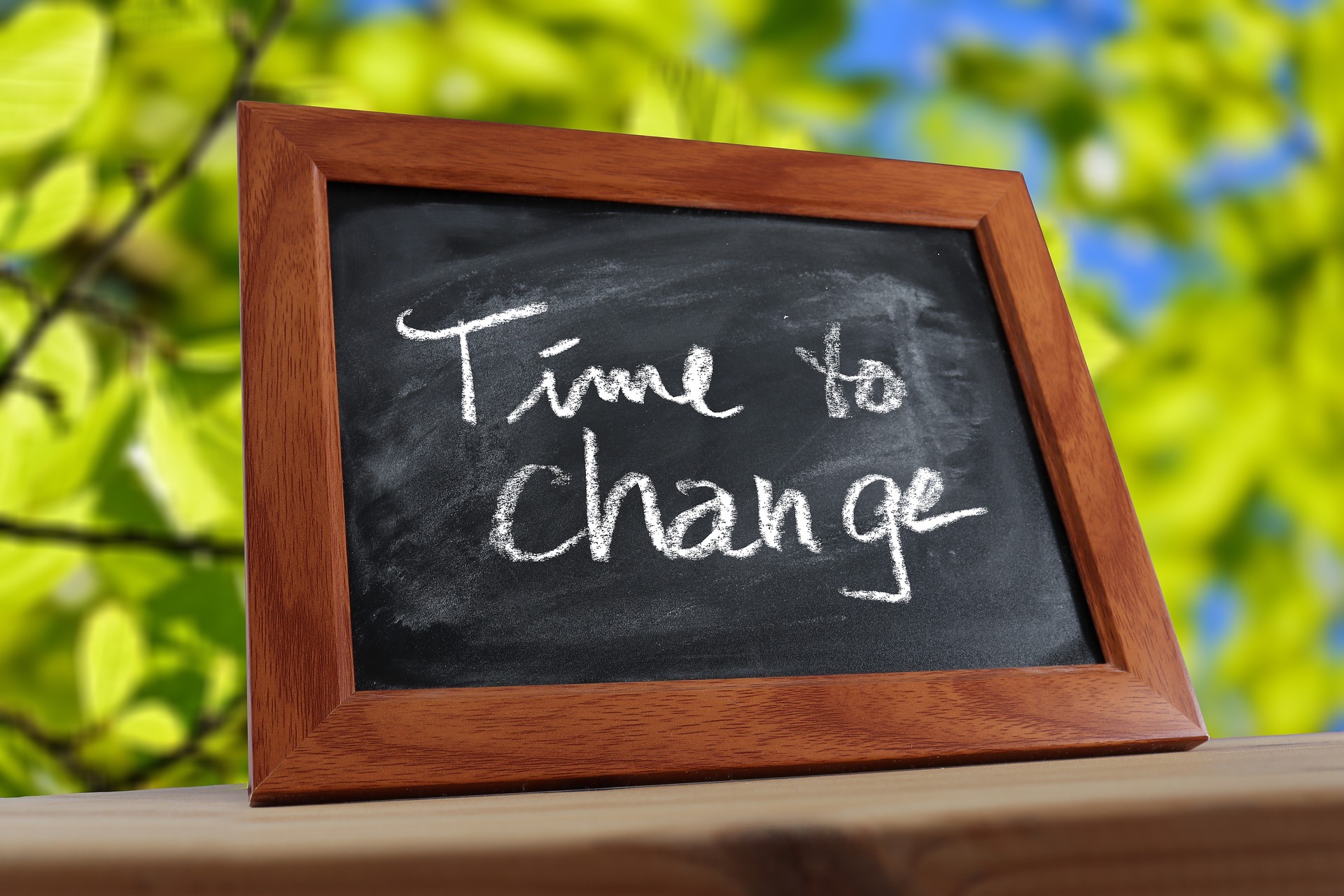 "Time to Change" Tischtafel (Schild) auf einem Holztisch im Freien. (Blätter der Baume sind im Hintergrund zu sehen)