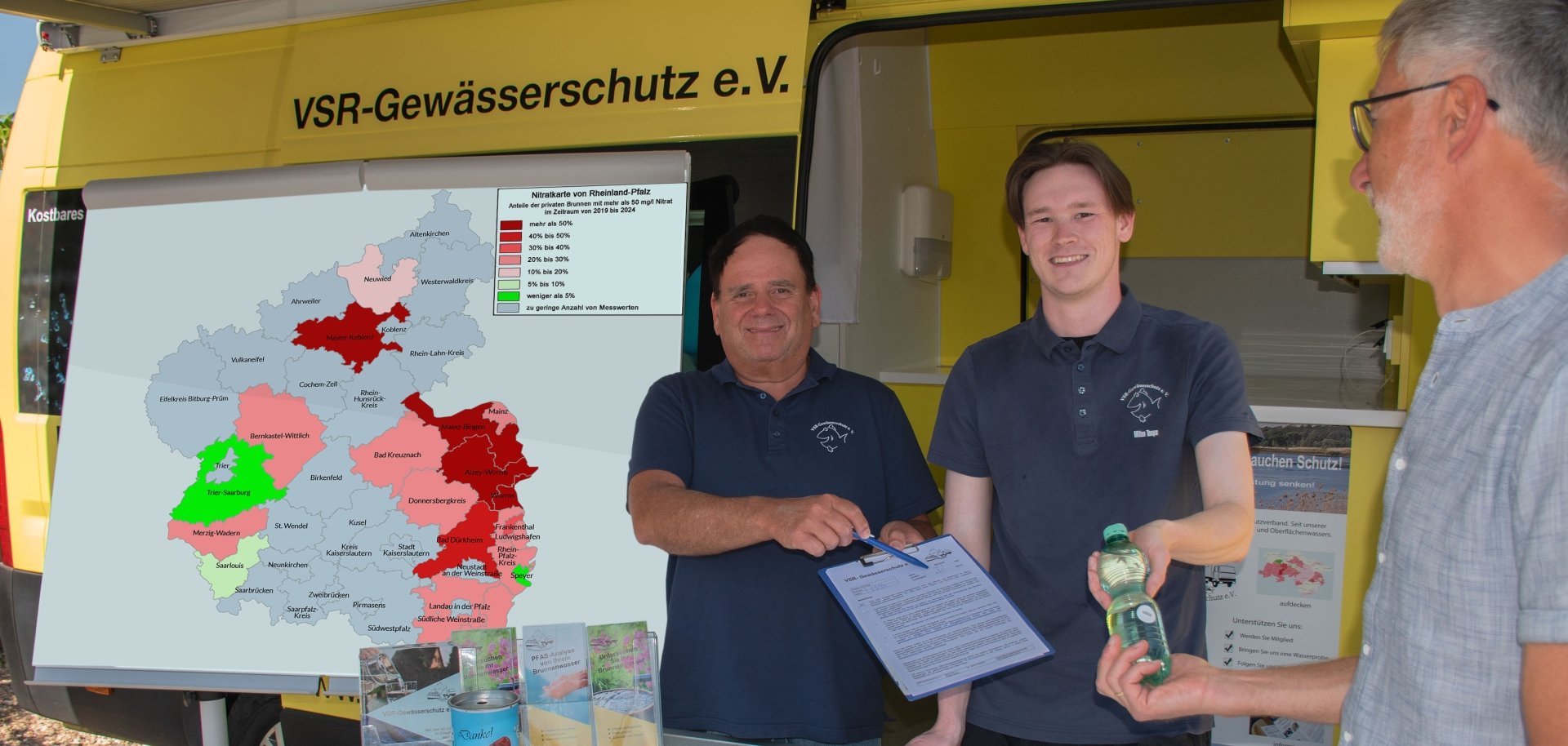 2 Männer geben einem anderen Mann eine flasche Wasser in die Hand