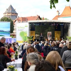 viele Menschen sitzen und auf der Bühne steht der Bürgermeister