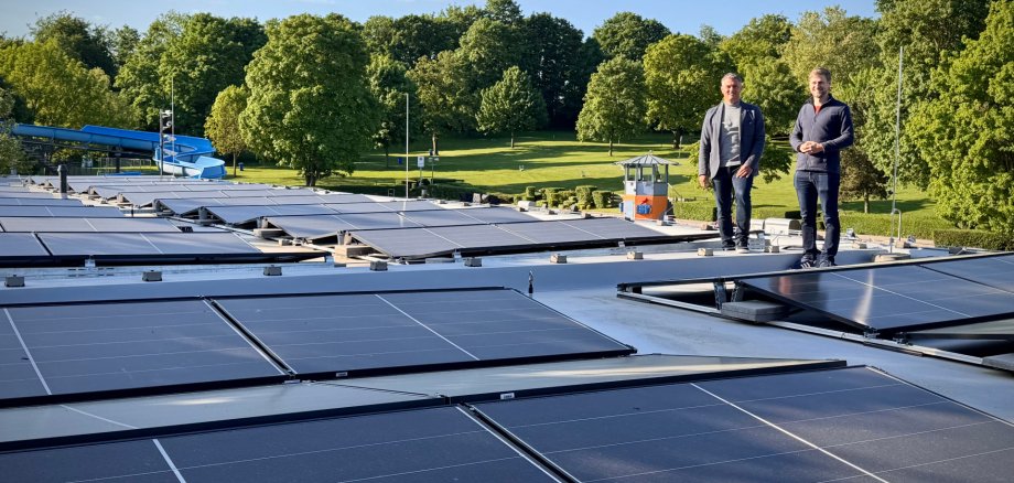 3 Männer stehen bei Solarplatten im Hintergrund ist die Schwimmbadrutsche