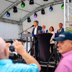 Auf dem Bild sind zwei Männer von hinten zu sehen, die Dr. Markus Merk fotografieren, welcher vor ihnen auf der Bühne steht und ins Mikrofon redet.