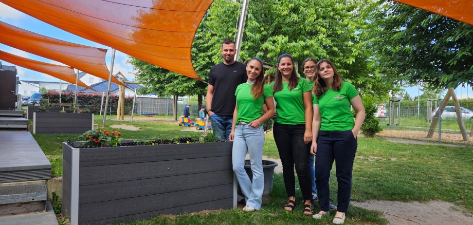 mehrere bepflanzte Hochbeete unter orangenen Sonnensegeln wurden fotografiert, vor diesen stehen fünf Personen in grünen Shirts, die alle in die Kamera lächeln