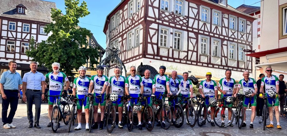 vor dem Alzeyer Roßmarkt-Brunnen stehen mehrere Rennradfahrer in  gleichem blau-weißen Anzug nebeneinander und schauen in die Kamera
