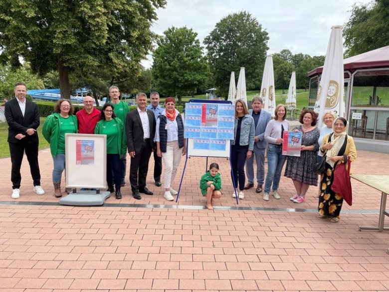 eine Gruppe von menschen steht gemeinsam mit Bürgermeister Streffen Jung im Alzeyer Wartbergbad, zwischen ihnen Plakataufsteller, einige Personen davon tragen grüne Shirts