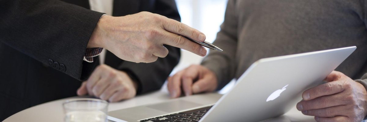Zwei Personen vor einem offenem Laptop. Ene Person zeigt mit dem Stift auf den Laptop.
