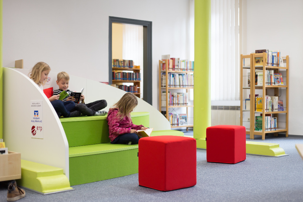 Kinder nutzen die Sitzgelegenheit in der Bücherei, um Bücher zu lesen