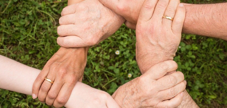 Personen fassen sich gegenseitig mit ihren Händen an das Handgelenk und bilden einen Kreis