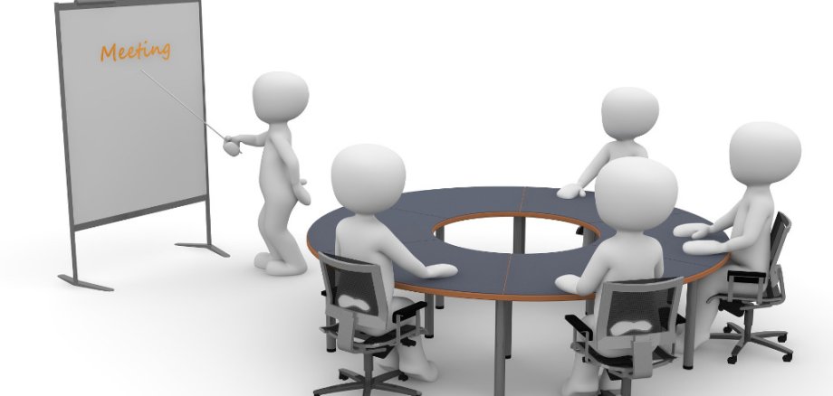Vier weiße Figuren sitzen an einem runden Tisch, eine wietere steht an einem Whiteboard