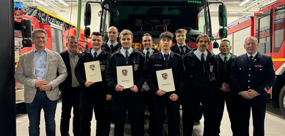 Eine Gruppe von Feuerwehrmännern steht mit Urkunden in der Hand vor einem Feuerwehrauto.