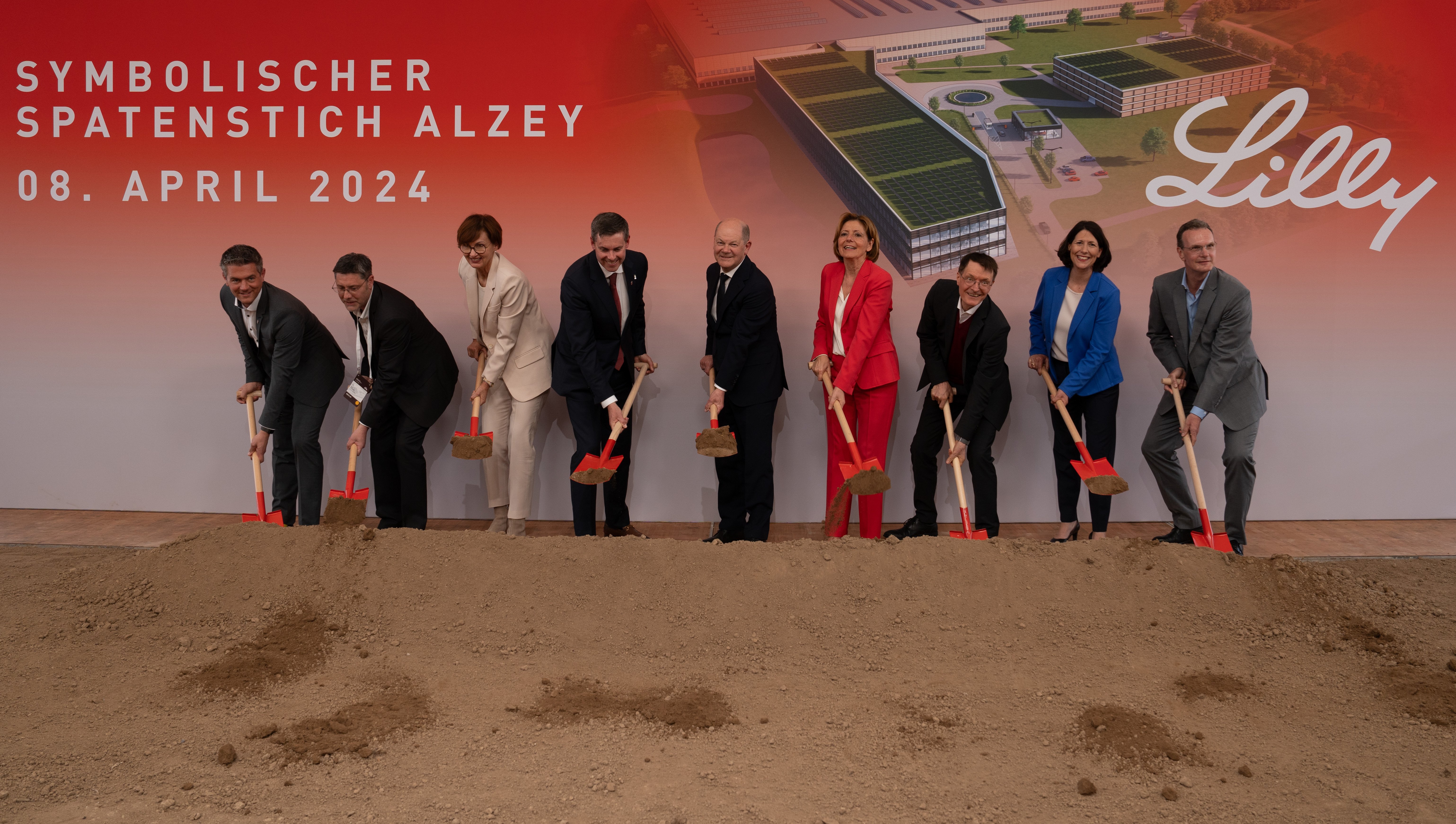 Neun Personen stehen mit Spaten in den Händen vor einer Stellwand, die das neue Firmengebäude von Eli Lilly in Alzey zeigt.